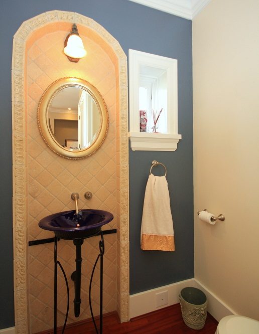 Bathroom with arched mirror, dark blue walls, and a pedestal sink. - 4069 West 37th Ave, Vancouver West Side
