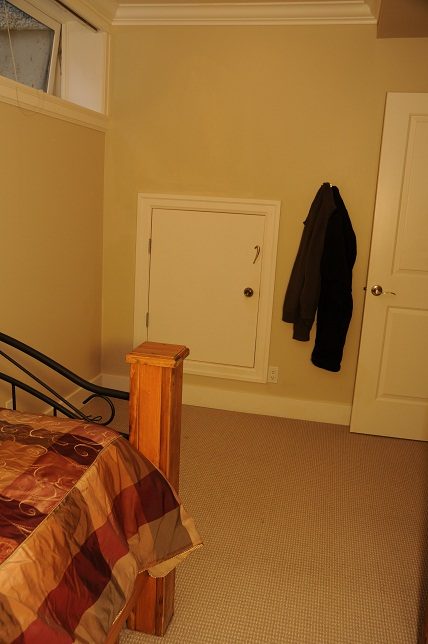 Furnished bedroom with a bed, wooden headboard, and a coat hanging on the wall. - 4069 West 37th Ave, Vancouver West Side