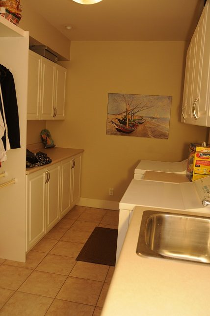 Bright kitchen with white cabinets, beige countertops, and a painting of boats on the wall. - 4069 West 37th Ave, Vancouver West Side