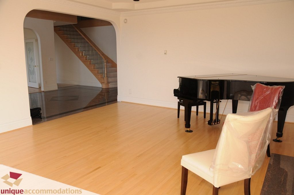 Bright living room with hardwood floors, piano, and staircase leading to upper levels. - 4139 Citadel Court, North Vancouver