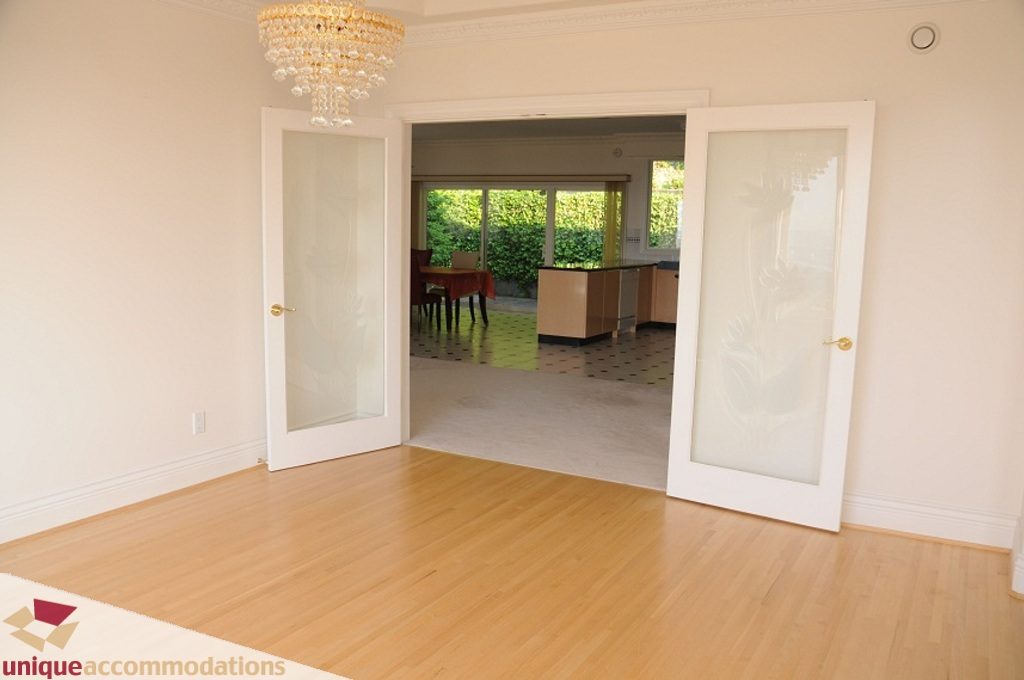 Bright living room with hardwood floors, chandelier, and sliding glass doors leading to outdoor patio. - 4139 Citadel Court, North Vancouver