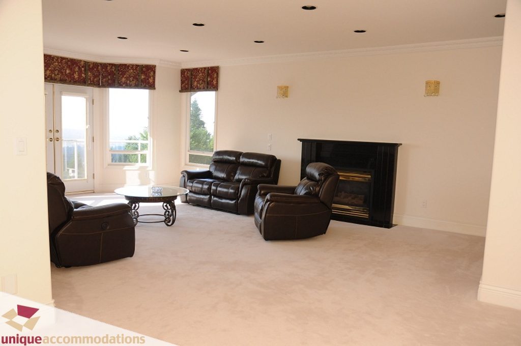 Spacious living room with large windows, leather recliners, and fireplace. - 4139 Citadel Court, North Vancouver