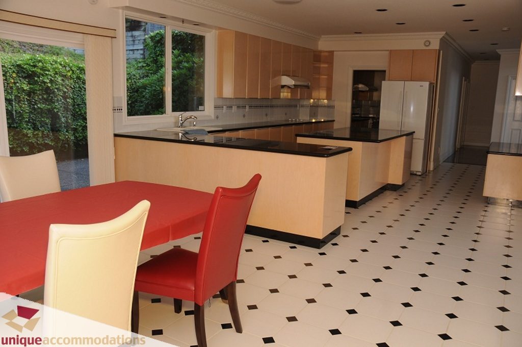 Bright kitchen with black countertops, white cabinets, and red chairs, featuring a checkered tile floor. - 4139 Citadel Court, North Vancouver