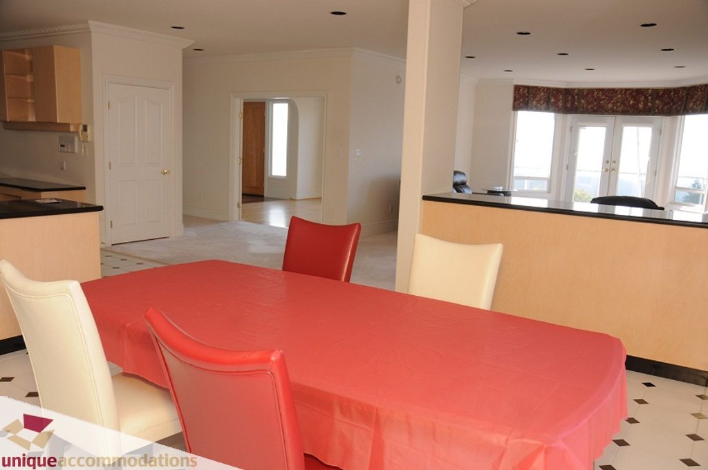 Furnished dining area with red tablecloth, white chairs, and city view through large windows. - 4139 Citadel Court, North Vancouver
