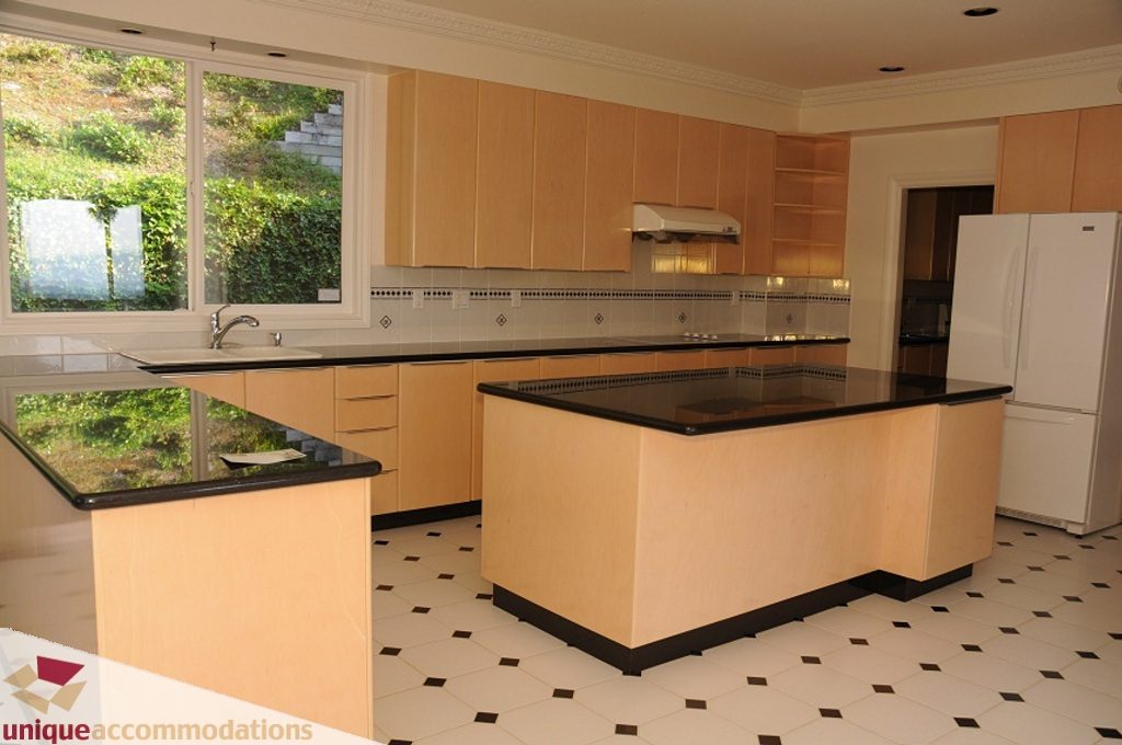 Bright kitchen with black countertops, light wood cabinets, and a view of greenery outside. - 4139 Citadel Court, North Vancouver