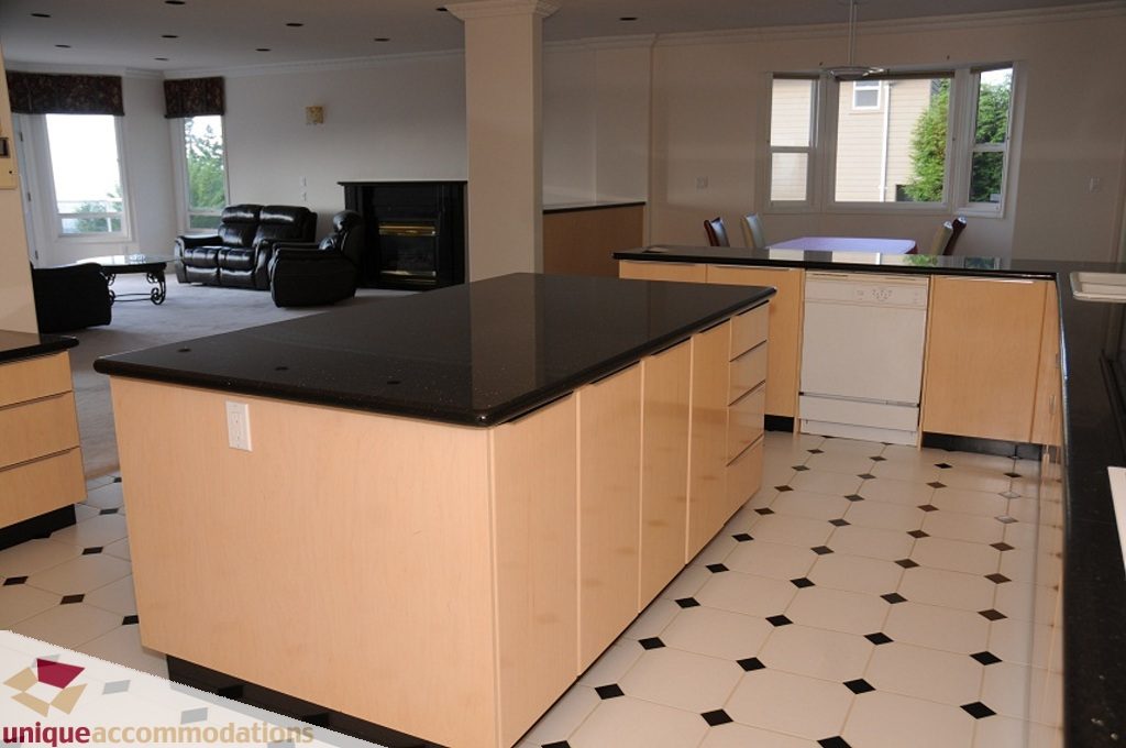 Bright kitchen with light wood cabinets, black countertops, and checkered floor tiles. - 4139 Citadel Court, North Vancouver