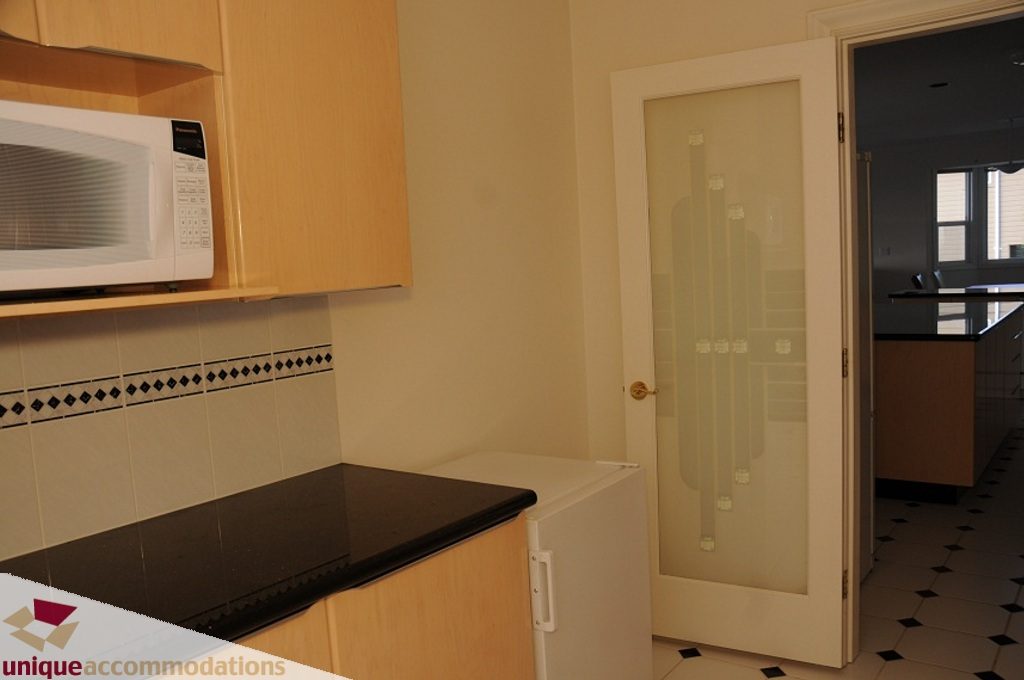 Bright kitchen with black countertops and white cabinets, leading to a glass-paned door. - 4139 Citadel Court, North Vancouver
