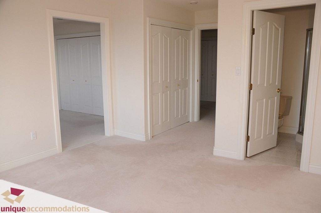 Large, empty bedroom with carpeted floor and white walls, leading to a bathroom and closet. - 4139 Citadel Court, North Vancouver