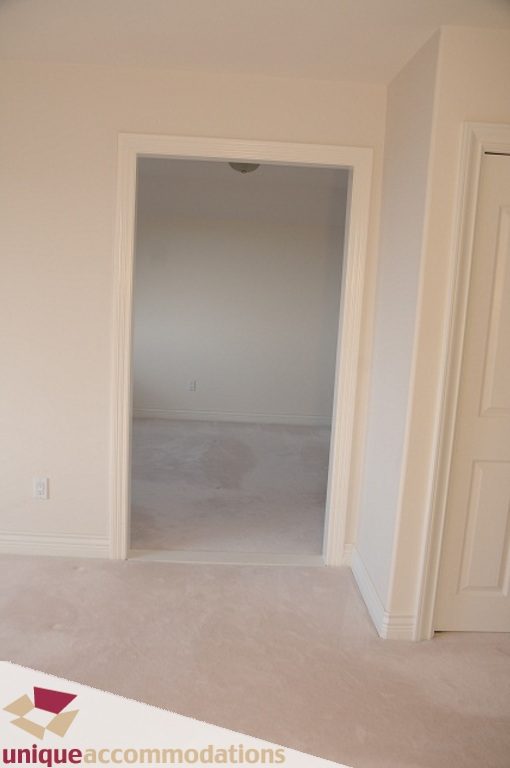 Bright hallway leading to a spacious bedroom with carpeted floors and white trim. - 4139 Citadel Court, North Vancouver
