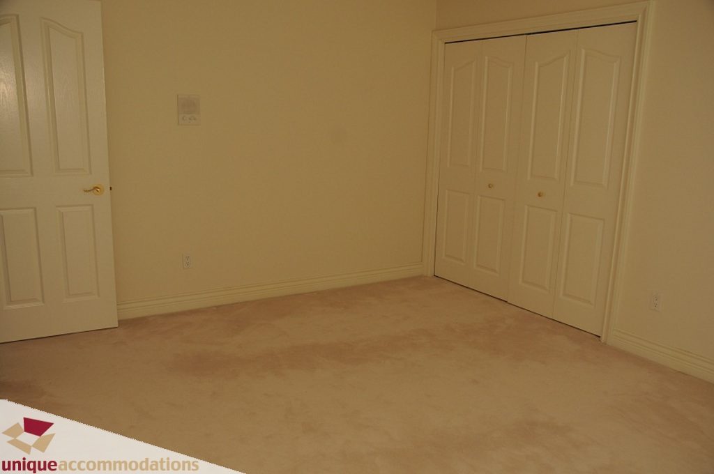 Empty bedroom with carpeted floor and white closet doors. - 4139 Citadel Court, North Vancouver