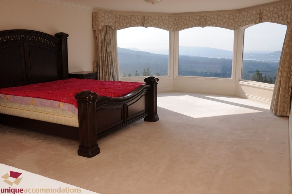 Spacious master bedroom with a large bed, red bedding, and a stunning mountain view. - 4139 Citadel Court, North Vancouver