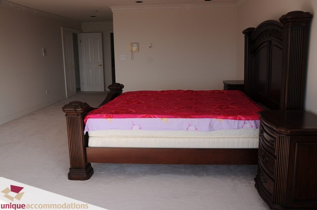 Master bedroom with a large bed, red and purple bedding, and a dark wooden headboard. - 4139 Citadel Court, North Vancouver
