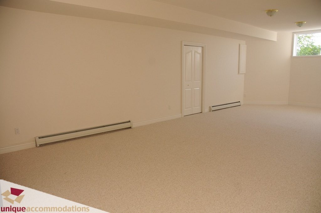 Empty living room with beige carpet and white walls, door and window visible. - 4139 Citadel Court, North Vancouver