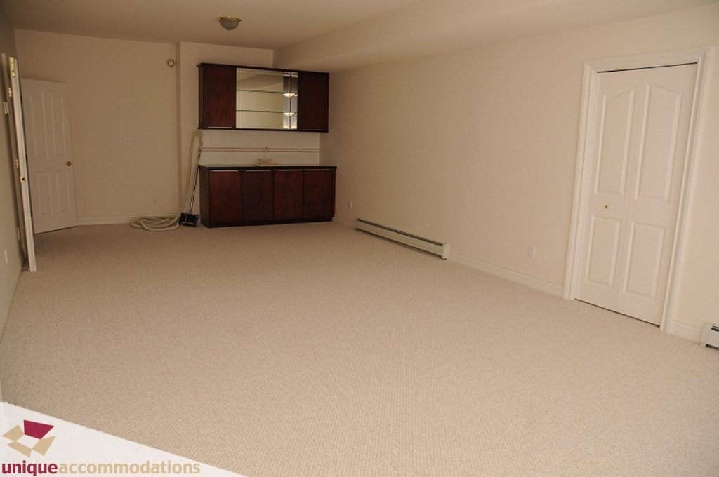 Empty living room with beige carpet and dark wood cabinet. - 4139 Citadel Court, North Vancouver