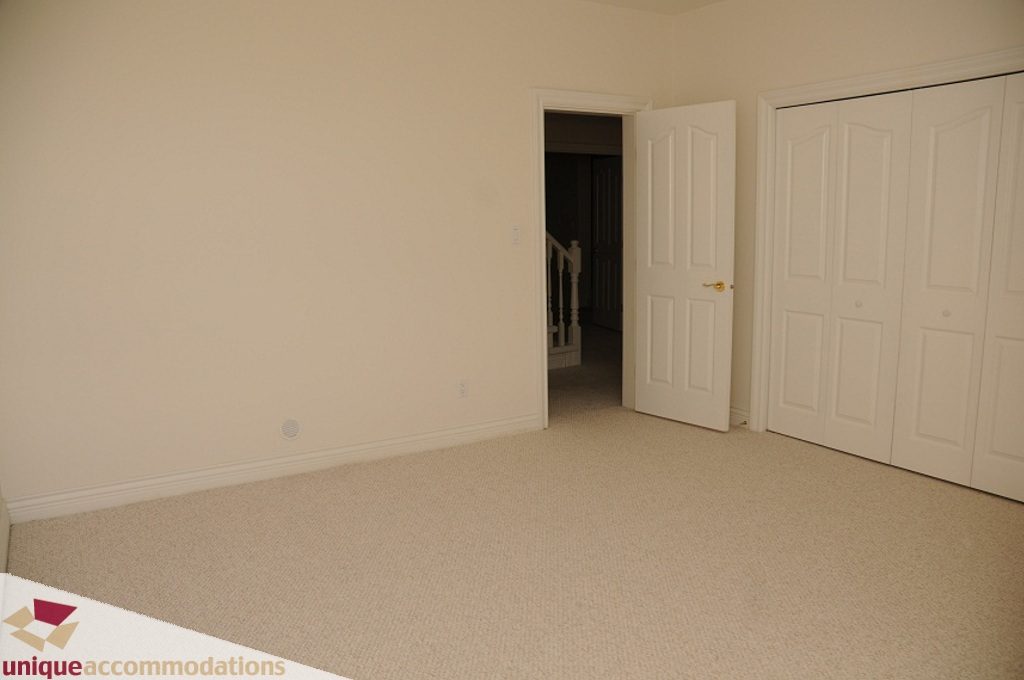 Large, empty bedroom with beige carpet and white closet doors. - 4139 Citadel Court, North Vancouver