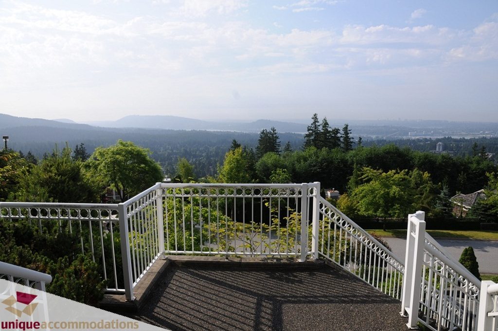 Furnished balcony with white railings, city view, and lush greenery. - 4139 Citadel Court, North Vancouver