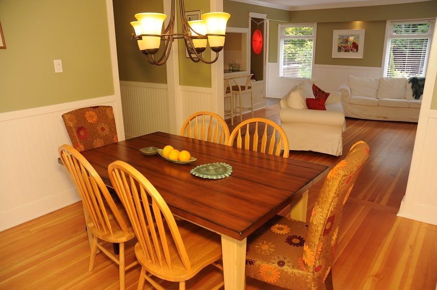 Dining room with wooden table, floral chairs, hardwood floors, and living room in background. - 6411 Nelson Avenue, West Vancouver
