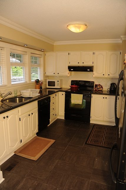 Bright kitchen with white cabinets, black countertops, and a view of the city through the window. - 6411 Nelson Avenue, West Vancouver