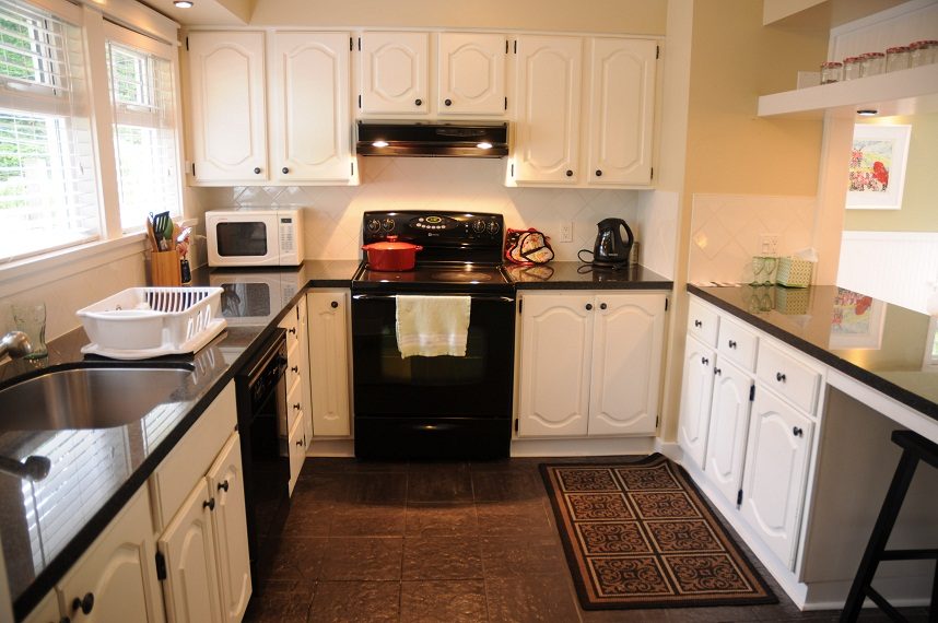 Bright kitchen with black countertops, white cabinets, and a red pot on the stove. - 6411 Nelson Avenue, West Vancouver