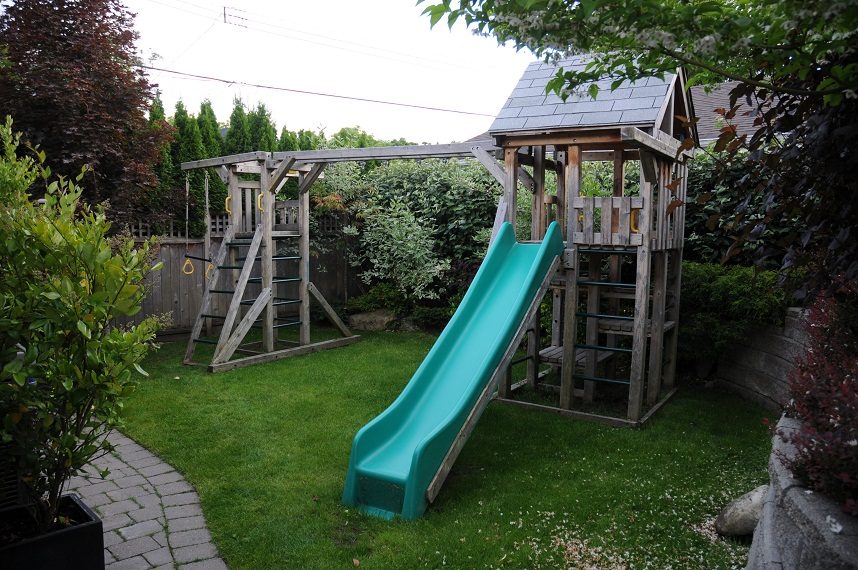 Playful backyard with a wooden play structure and a vibrant green slide. - 4104 West 12th Avenue, Vancouver West Side