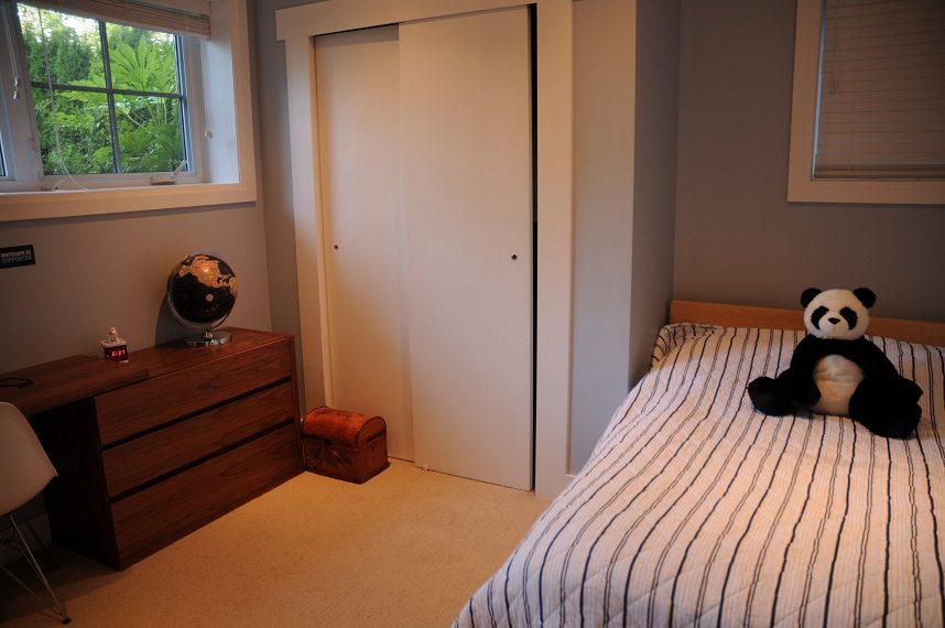 Bright bedroom with striped bedding and a panda plush, featuring a wooden dresser and a sliding closet door.