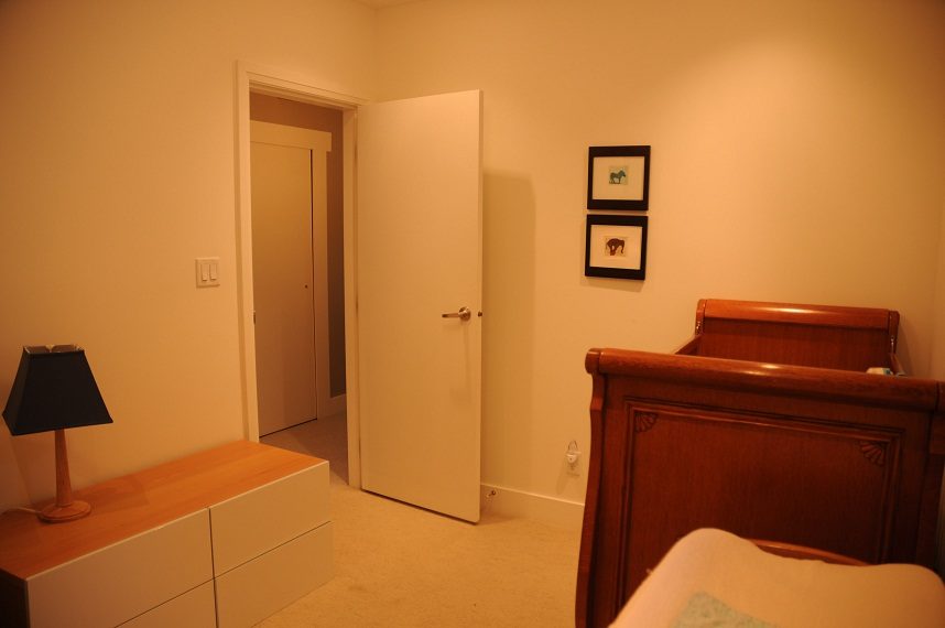 Furnished bedroom with wooden sleigh bed and black lamp, leading to another room. - 4104 West 12th Avenue, Vancouver West Side