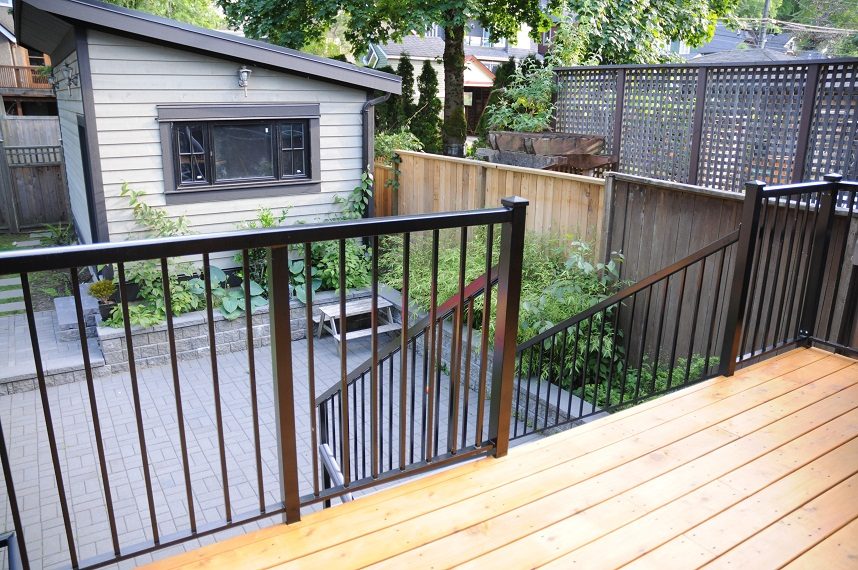 Furnished deck with wooden flooring and black railing, leading to a patio area. - 4104 West 12th Avenue, Vancouver West Side