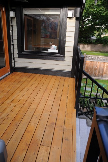 Furnished deck with wooden flooring and black railings, leading to a cozy interior with a window view. - 4104 West 12th Avenue, Vancouver West Side