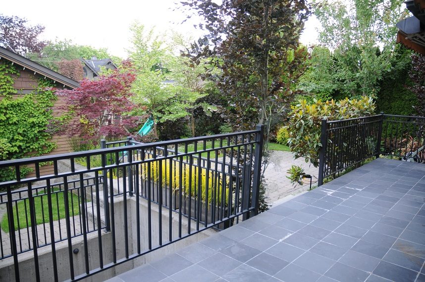 Furnished patio with black railing and stone flooring, surrounded by lush greenery. - 4104 West 12th Avenue, Vancouver West Side