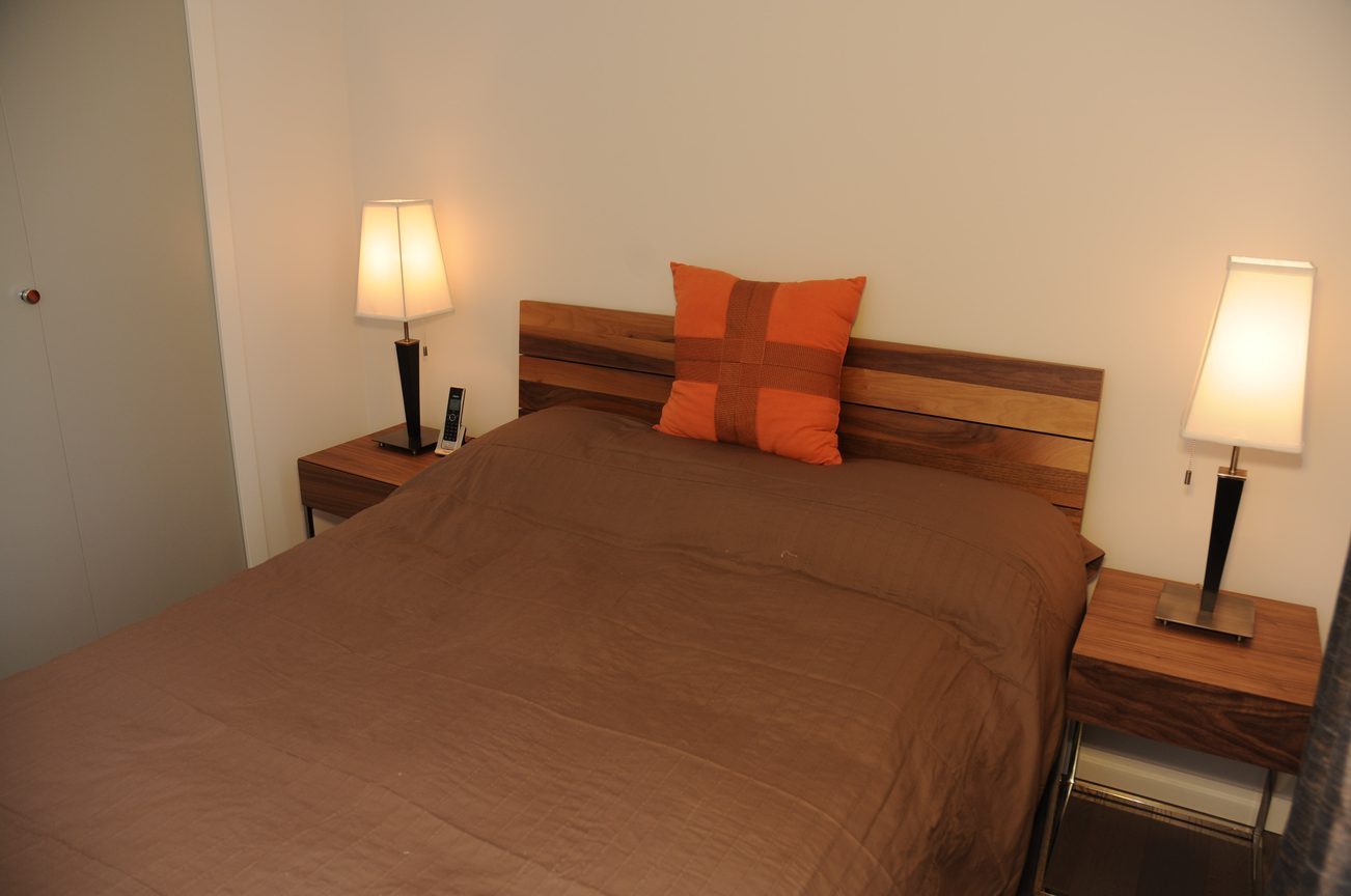 Furnished bedroom with wooden headboard, brown bedding, and orange accent pillow. - 801 - 161 West Georgia, Vancouver Downtown