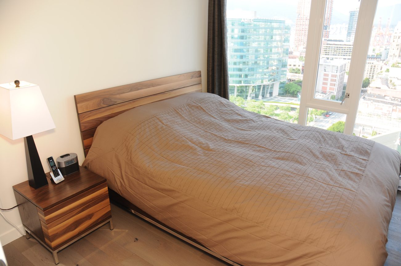 Bright bedroom with wooden bed, city view, and hardwood floors. - 2201 - 161 West Georgia, Vancouver Downtown
