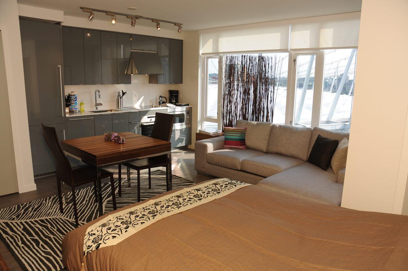 Bright kitchen with modern appliances and city view, featuring a cozy living area with a sectional sofa and hardwood floors.