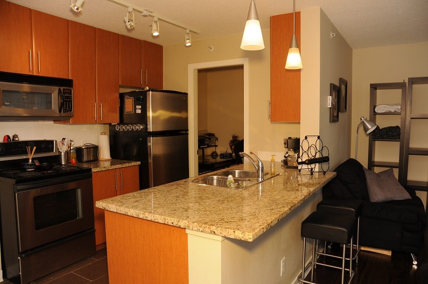 Bright kitchen with granite countertops and stainless steel appliances, open to a cozy living area with a black sofa.