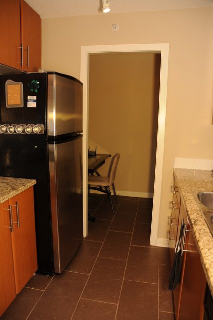 Bright kitchen with granite countertops and stainless steel appliances, leading to a dining area with a chair and table.
