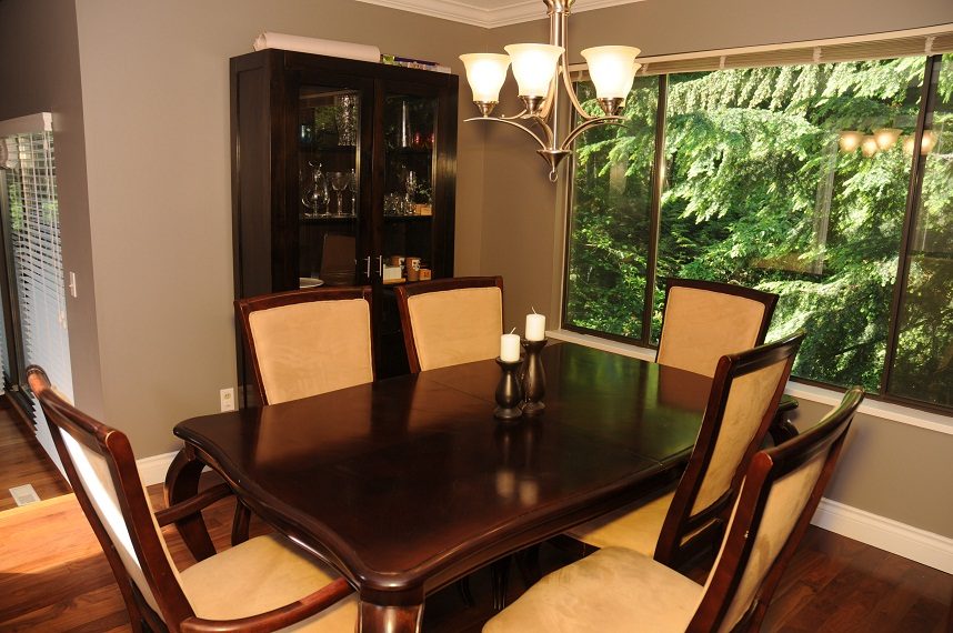 Dining room with dark wood table, cream chairs, and large windows showing greenery. - 5591 Huckleberry Place, North Vancouver