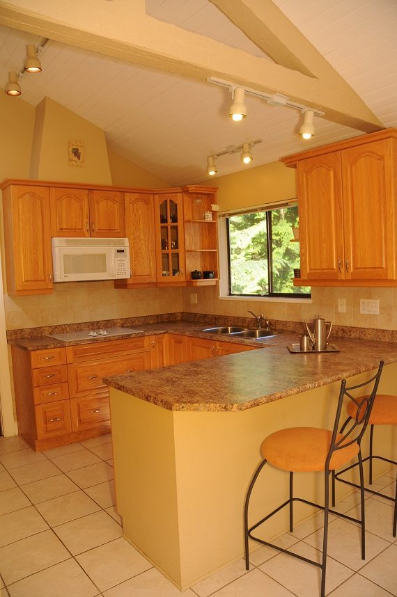 Bright kitchen with granite countertops, wooden cabinets, and a large window. - 5591 Huckleberry Place, North Vancouver