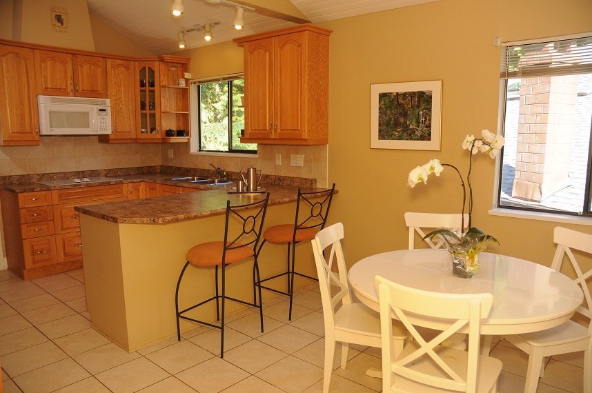 Bright kitchen with granite countertops, wooden cabinets, and a dining area with a round table and white chairs.