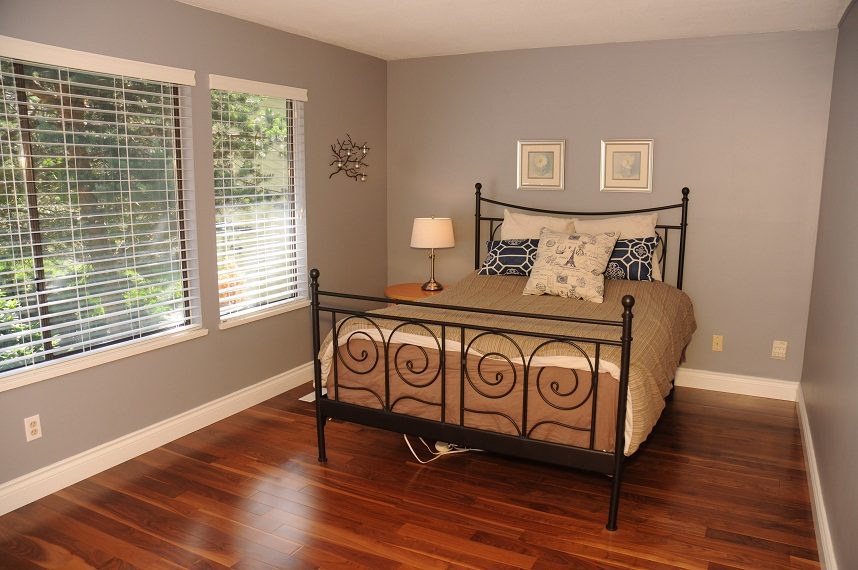 Furnished bedroom with hardwood floors, large windows, and a metal bed frame. - 5591 Huckleberry Place, North Vancouver