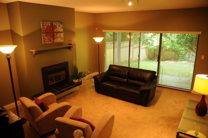 Furnished living room with a fireplace, leather couch, and sliding glass doors to a backyard. - 5591 Huckleberry Place, North Vancouver