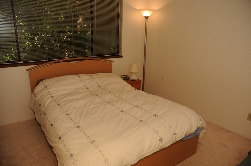 Furnished bedroom with wooden headboard and white bedding, natural light from window. - 5591 Huckleberry Place, North Vancouver