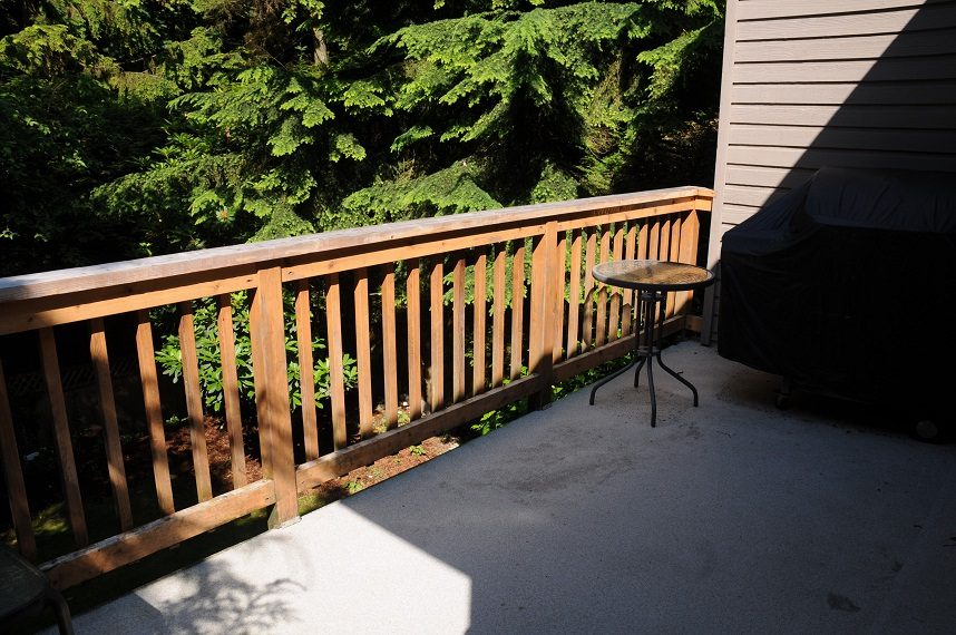 Furnished patio with wooden railing and outdoor table, surrounded by lush greenery. - 5591 Huckleberry Place, North Vancouver