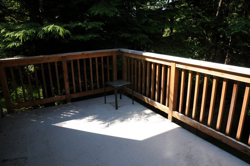 Spacious deck with wooden railing and concrete floor, surrounded by lush greenery. - 5591 Huckleberry Place, North Vancouver