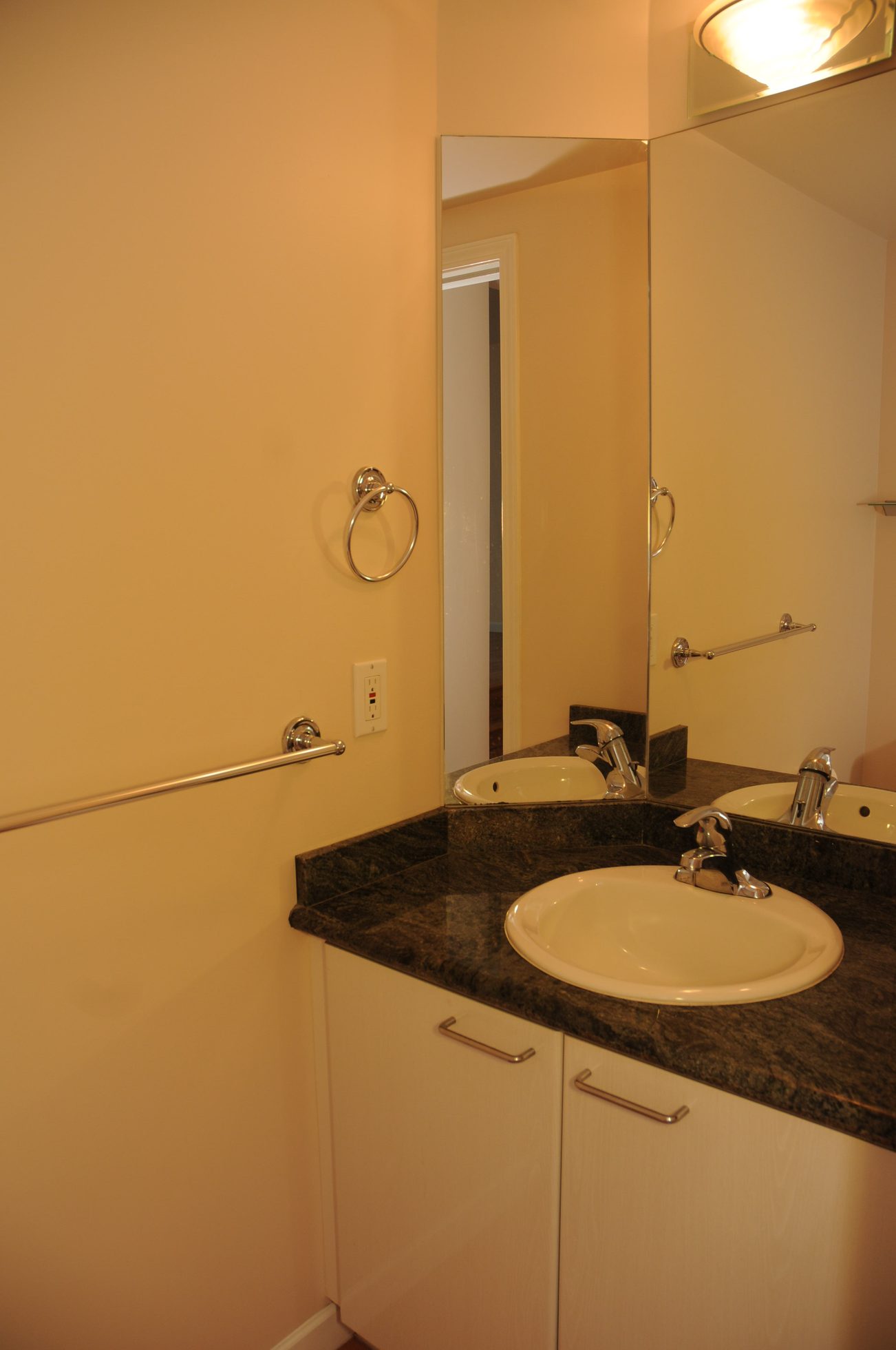 Bathroom with dual sinks, granite countertop, and wall-mounted towel ring. - 211 - 1166 Melville St, Vancouver Downtown