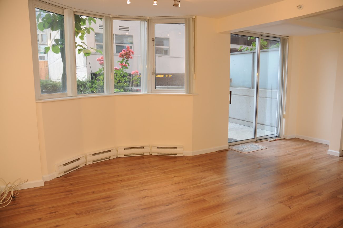 Bright living room with hardwood floors and large windows, leading to a patio. - 211 - 1166 Melville St, Vancouver Downtown
