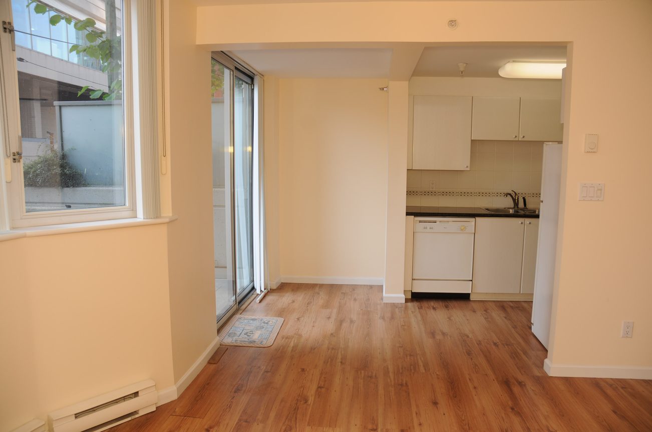Bright kitchen with hardwood floors and white cabinets, leading to a cozy living area with a sliding glass door.