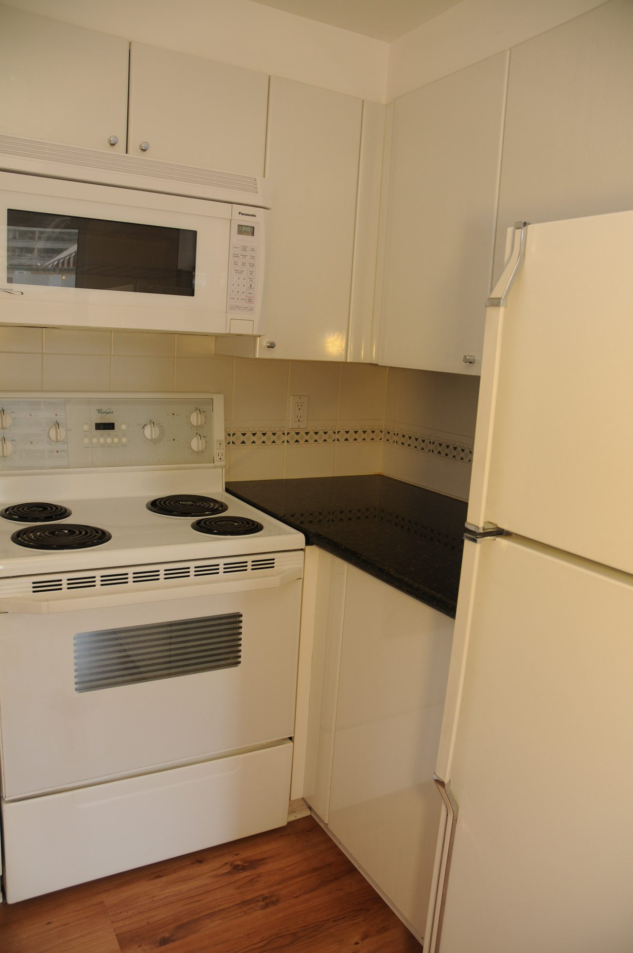 Bright kitchen with black countertops, white cabinets, and hardwood floors. - 211 - 1166 Melville St, Vancouver Downtown