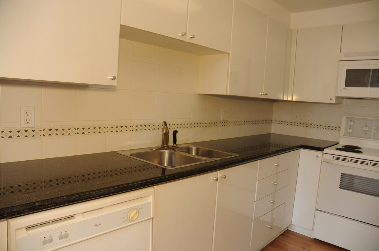 Bright kitchen with black countertops and white cabinets, featuring a double sink and a microwave above the stove.