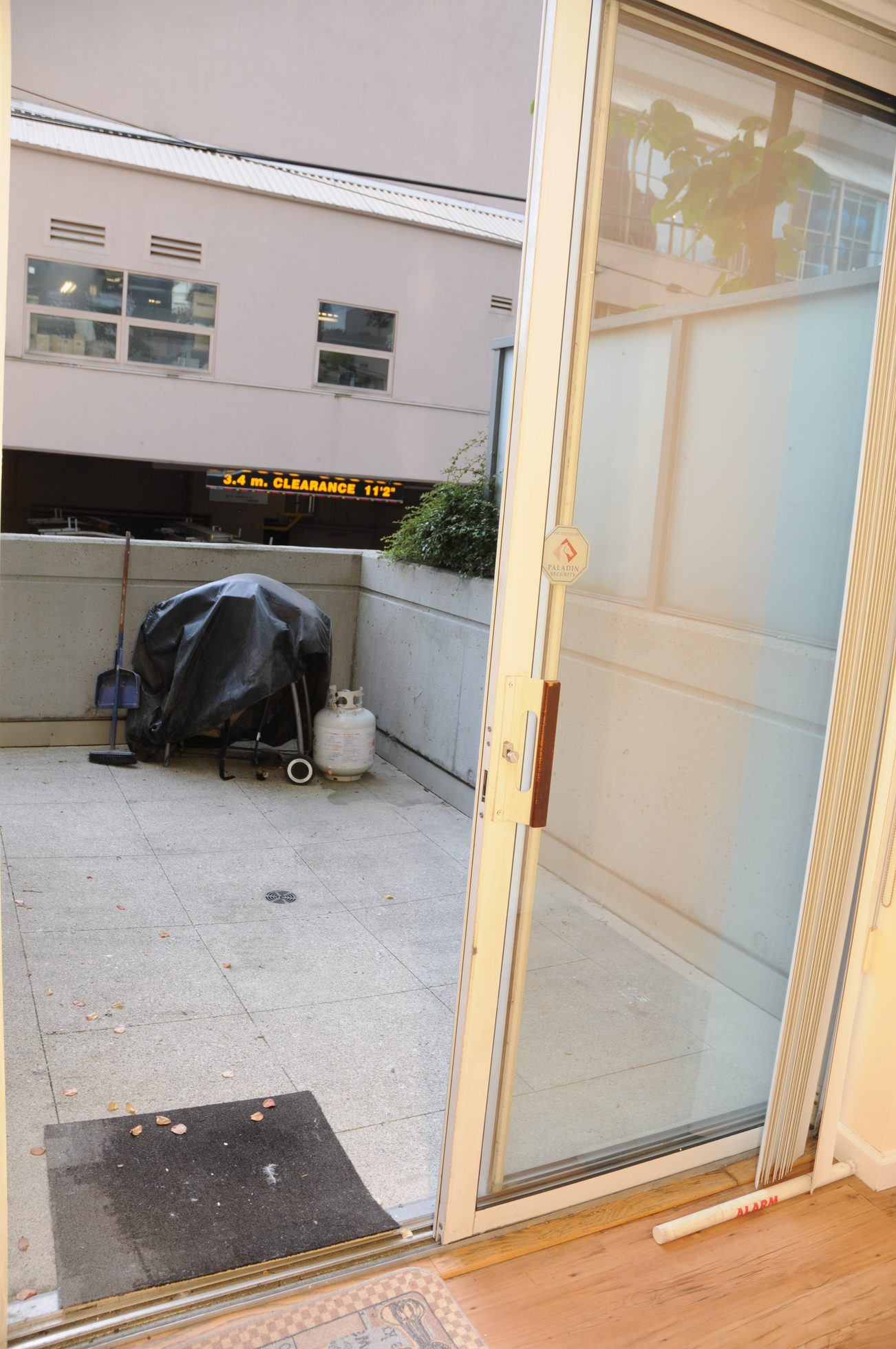 Furnished entryway with glass door, hardwood floor, and outdoor patio area with a propane tank and broom. - 211 - 1166 Melville St, Vancouver Downtown