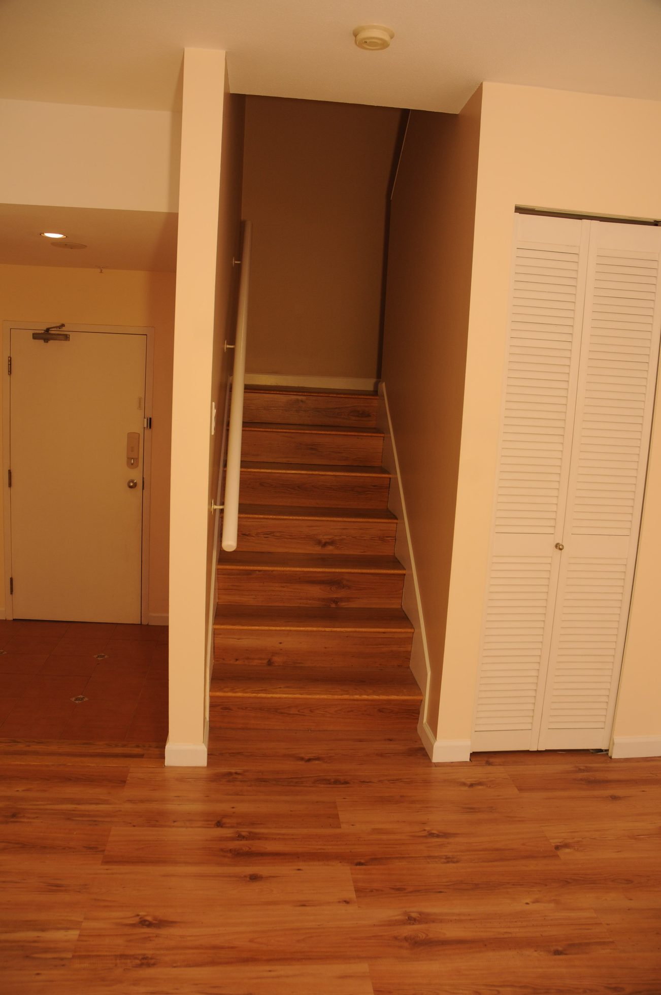 Bright hallway leading to stairs with hardwood floors and white closet doors. - 211 - 1166 Melville St, Vancouver Downtown