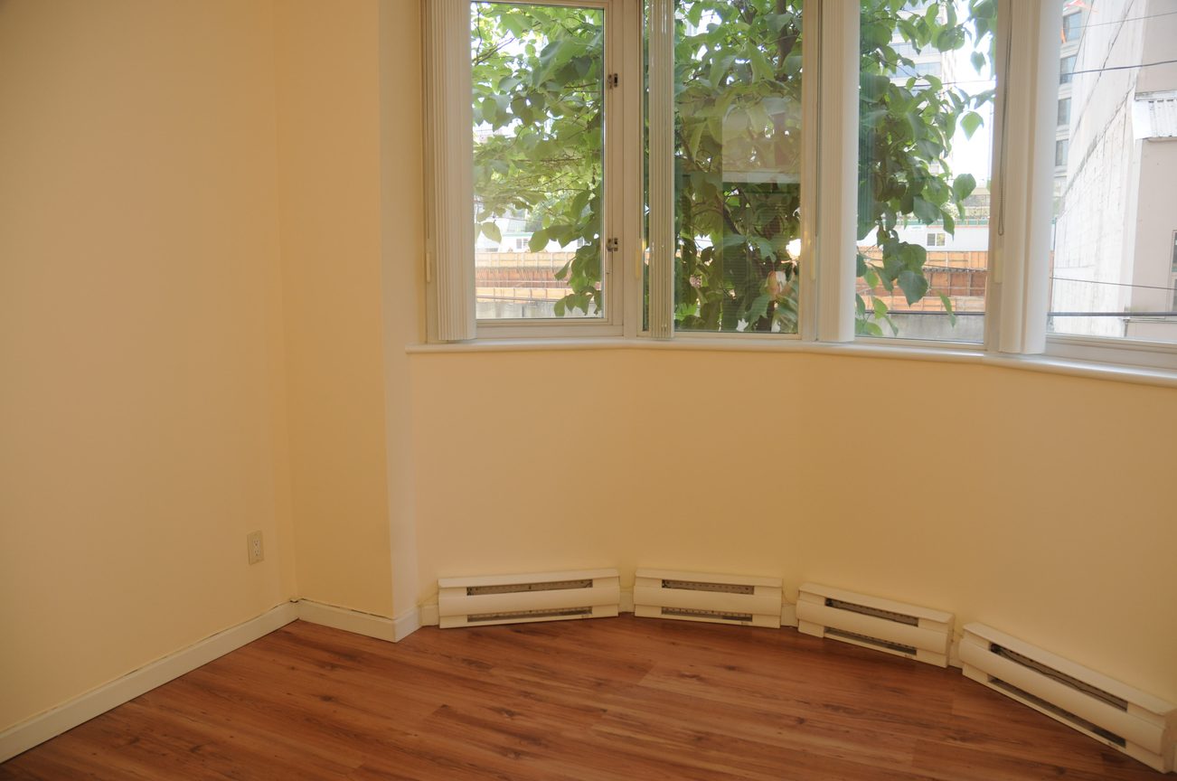 Bright living room with hardwood floors and large windows, offering a city view. - 211 - 1166 Melville St, Vancouver Downtown